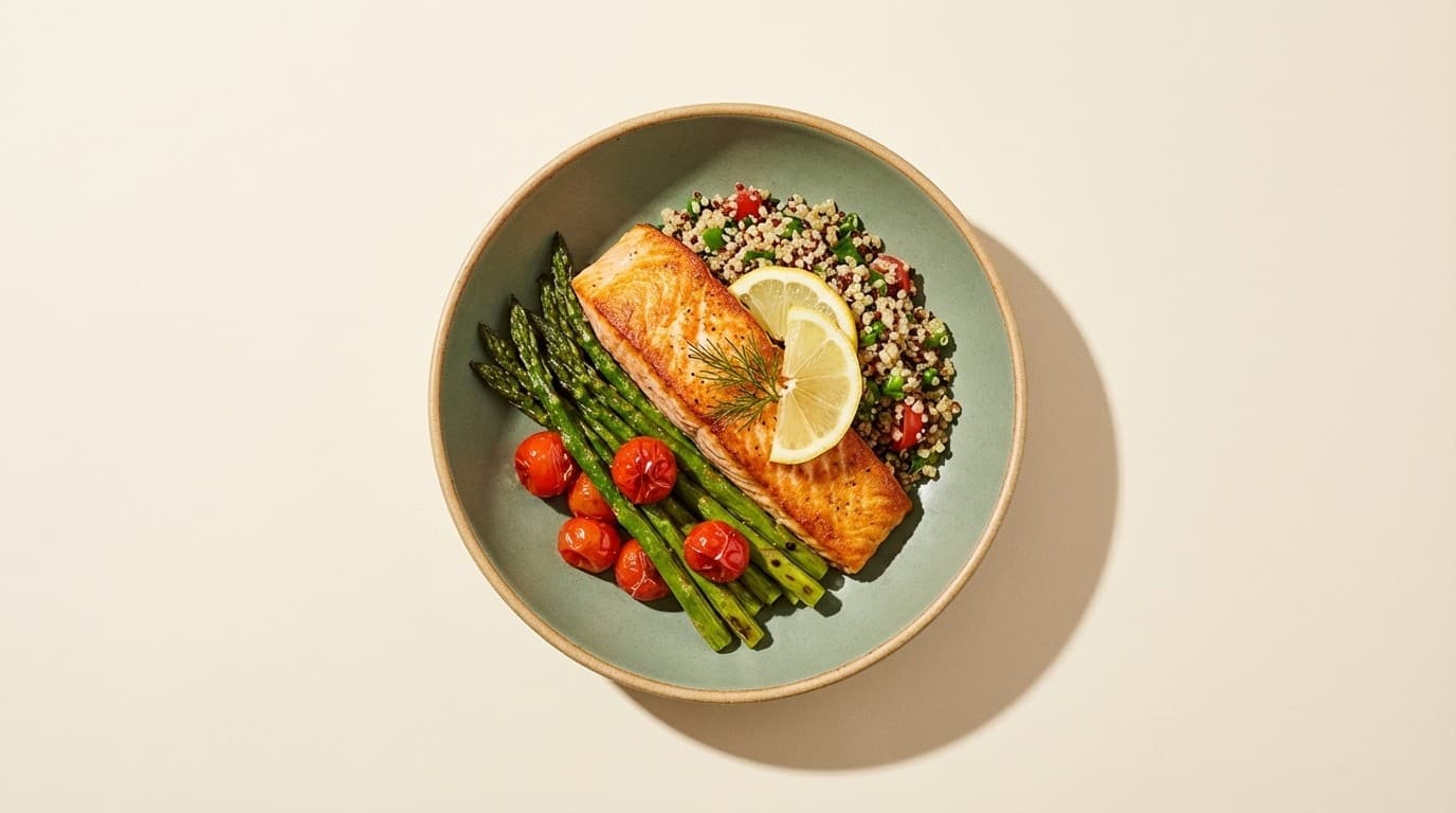 A bowl seen from above: seared salmon with dill and lemon, green asparagus, roasted cherry tomatoes and a grain salad.